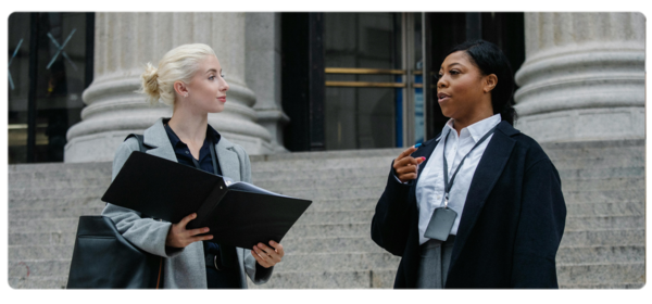 Two professionals have a conversation on the steps of a government building.