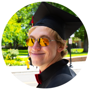 Graduate in orange reflective sunglasses smiles at the camera.